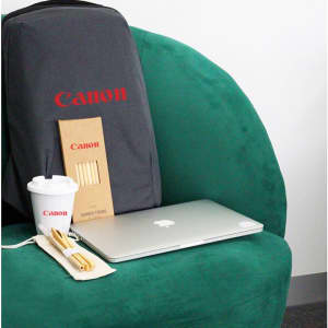 A grey backpack with a logo, a laptop, a coffee cup, and a wooden straw set on a green chair.