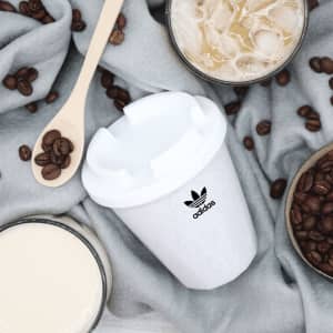 A drink bottle with a white exterior and a logo, surrounded by coffee beans and glasses of iced drinks.