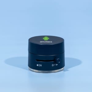 A black and silver device with a logo on top and a dial on the side, resting on a blue background.