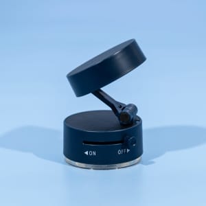 A black and silver vacuum suction phone stand with a rotating top and an on/off switch. It features a logo.