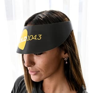 A black sun visor with a logo, worn by a woman with long hair, indoors against a light background.