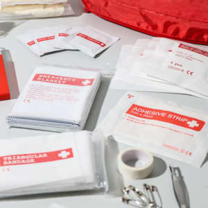 A red first aid kit containing various items, including an emergency blanket, adhesive strips, triangular bandages, and more.
