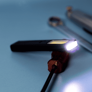 A rechargeable work light in black with a bright white LED, placed on a blue surface alongside tools.