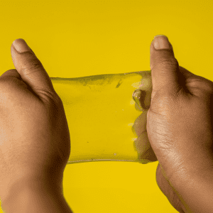 A pair of hands stretching a translucent yellow jelly cube sensory toy against a bright yellow background.