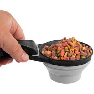 A collapsible silicone pet food scoop in black and grey, filled with colourful pet food, held in a hand.
