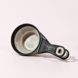 A black and grey collapsible silicone pet food scoop with a bag clip, featuring a logo.