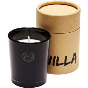 A black glass candle with a white wick, packaged in a round brown cardboard container. Features a logo.