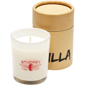 A white glass candle in a clear holder, placed next to a kraft paper gift box.
