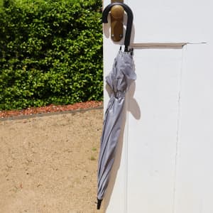 A grey umbrella hanging on a door handle, featuring a curved black handle.