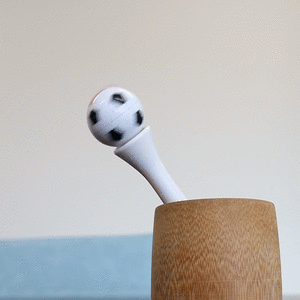 A white pen with a spinning soccer ball topper, placed in a wooden holder.