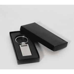 A silver keychain displayed inside a black box. The keychain has a rectangular shape with a polished finish.