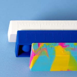 Three popper rulers in vibrant colours: a white ruler, a blue ruler, and a multicoloured patterned ruler, stacked together.