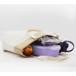 A jute and cotton cooler bag in cream and tan containing a drink bottle, a lunchbox, and an apple.