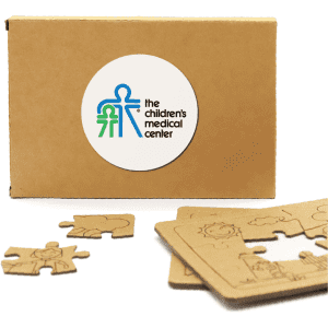 A cardboard box containing wooden jigsaw puzzle pieces, featuring a logo and light brown tones.
