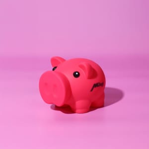 A pink pig-shaped money box with a small logo on its side, set against a pink background.