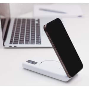 A white power bank with a wireless charging feature and a smartphone in the process of being charged.