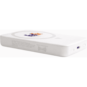 A white wireless charging power bank with a logo, resting on a desk near plants and a laptop.