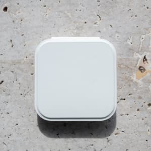 A white compact mirror with an LED light, featuring a square shape and a smooth surface, resting on a textured stone background.