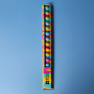 A 30cm popper ruler featuring a vibrant design with blue and multicoloured dots, alongside a logo.