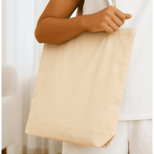 A neutral-toned tote bag held by a person, featuring a simple design and an attached logo.
