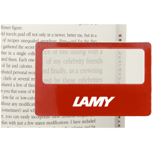 A red pocket ruler magnifier with a clear lens, placed over text in a book, featuring a logo.