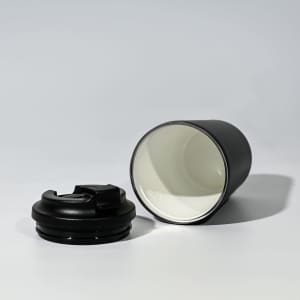 A travel cup in black with a removable lid, featuring a stainless steel inner lining and a sleek design.