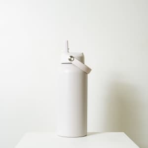 A drink bottle in a soft white finish with a screw-top lid and a handle, featuring a simple logo.