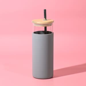A drink bottle with a grey silicone sleeve, clear glass body, and wooden lid, featuring a reusable straw.