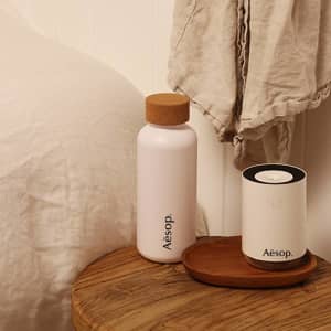 A drink bottle in pale pink with a cork lid, displayed on a wooden table alongside a white cylindrical object.