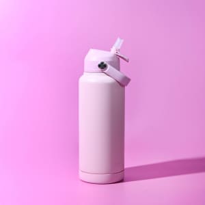 A drink bottle in a soft pink colour with a flip-top lid and a strap. It features a logo on the side.
