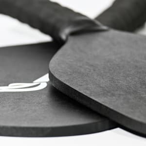 A black pickleball paddle and ball set with a textured grip, featuring a logo on one item.