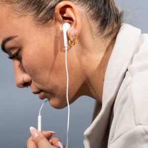 A woman with light skin has white USB Type C earphones in her ears, with soft lighting and a neutral background.