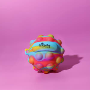 A vibrant, multicoloured stress ball with a textured surface and a logo. It rests on a pink background.