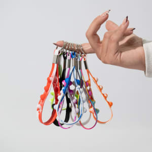 A hand holding multiple Popper Stress Reliever Key Chains in various bright colours. The keychains include a variety of playful designs.
