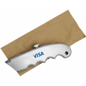 A silver cutter with a textured grip, resting on a piece of brown paper. The cutter features branding.