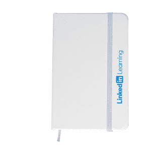 A white A6 notebook with a blue elastic band and branding on the side.