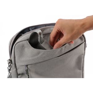 A grey business sling laptop bag with a hand reaching into an outer pocket. It features a sleek design and a logo.