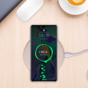 A wireless charger featuring a wheat straw design, paired with a smartphone displaying a charging status, on a wooden surface.