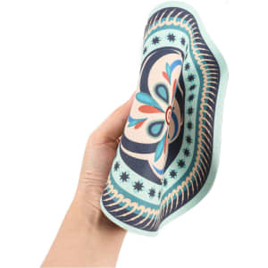 A patterned, heat-resistant trivet in shades of blue, green, and cream held in a hand. Features a decorative design and a logo.
