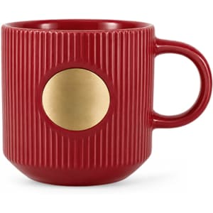 A red ceramic mug with a ribbed design and a bronze medal emblem on the side. It has a curved handle.