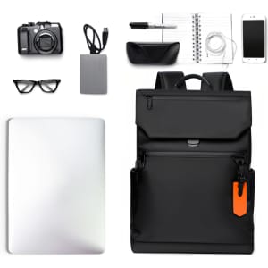A black flap laptop backpack surrounded by a camera, notebook, glasses, charger, pen, phone, and external drive.