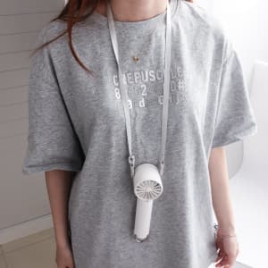 A person wearing a grey oversized t-shirt with a white high-speed cooling fan hanging around their neck.
