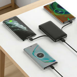 A black 5000mAh slim power bank with charging cables, connected to two smartphones on a table.