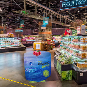 A round fitted table cover featuring a blue design with tomatoes, placed in a supermarket produce area.