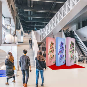 A pink and blue straight fabric popup display stands in a modern exhibition space with stairs and escalators in view.