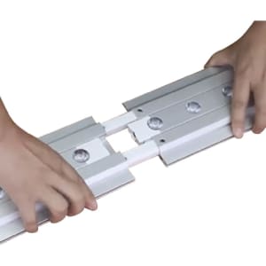 Two hands assembling components of a backlit LED light box display, featuring silver and white parts.
