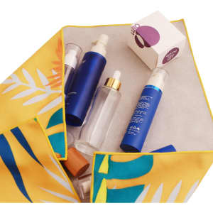 A vibrant yellow and green cloth holds various blue and clear spray bottles alongside a small white box.