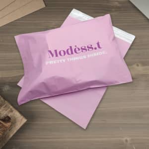 A pink biodegradable mailer bag with a logo on the front, resting on a wooden surface.