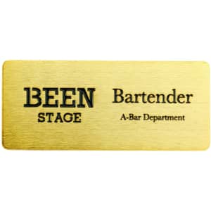 A metal name badge in a gold finish, featuring black text with a logo on one side.