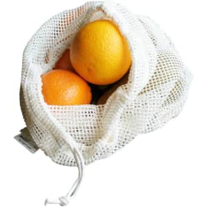 A white organic cotton mesh bag containing three oranges, with a drawstring closure and a visible logo.